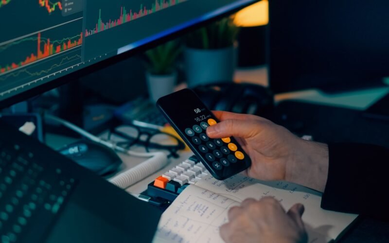 Business analysis with calculator and computer monitor displaying financial graphs and charts.