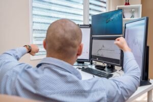 A man celebrates success at a multi-monitor workstation while analyzing stock charts.