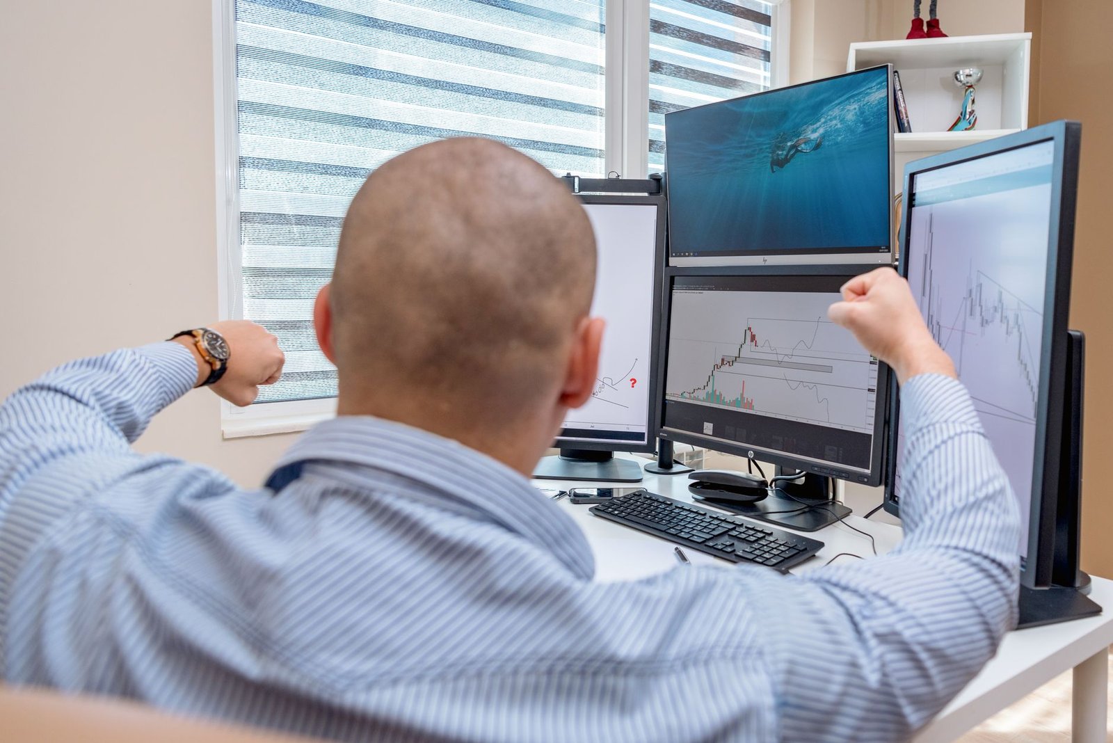 A man celebrates success at a multi-monitor workstation while analyzing stock charts.