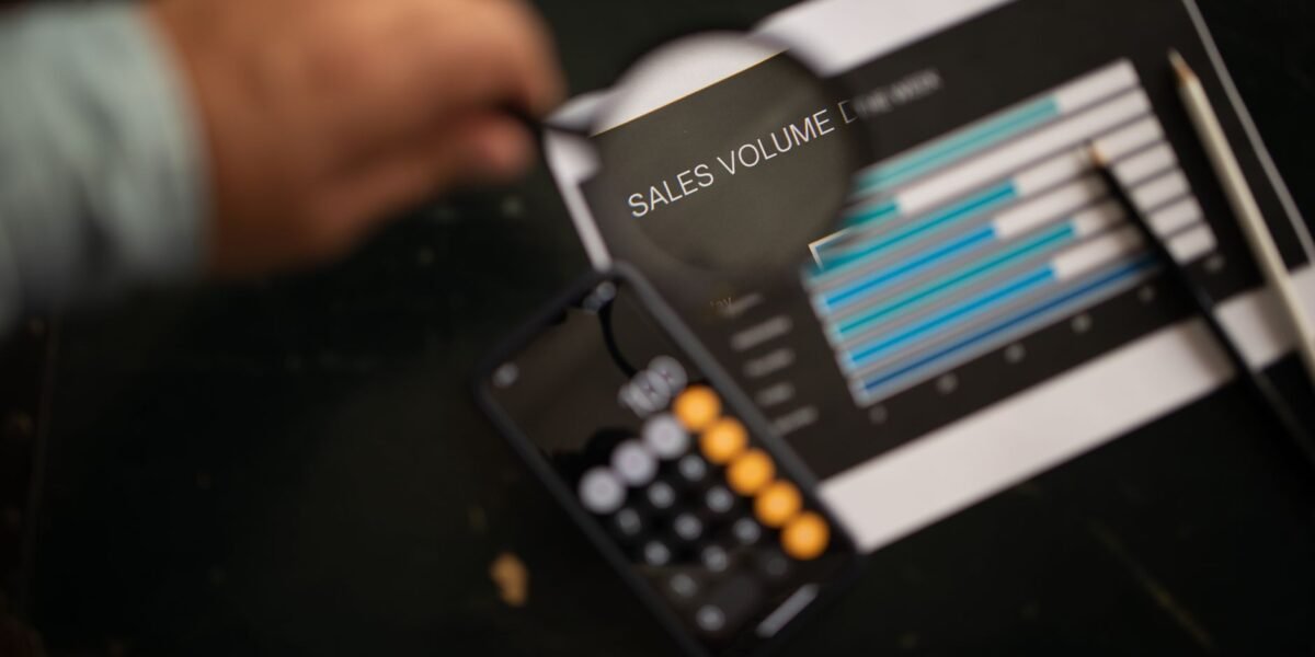A focused examination of sales volume data using a magnifying glass and calculator.