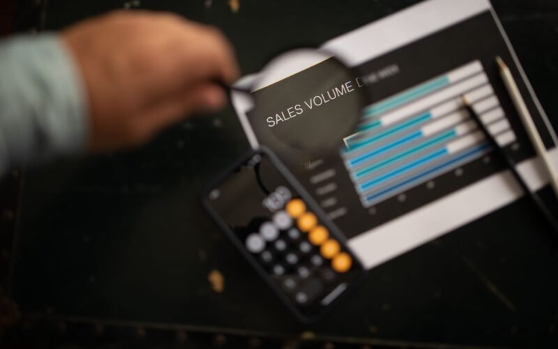 A focused examination of sales volume data using a magnifying glass and calculator.