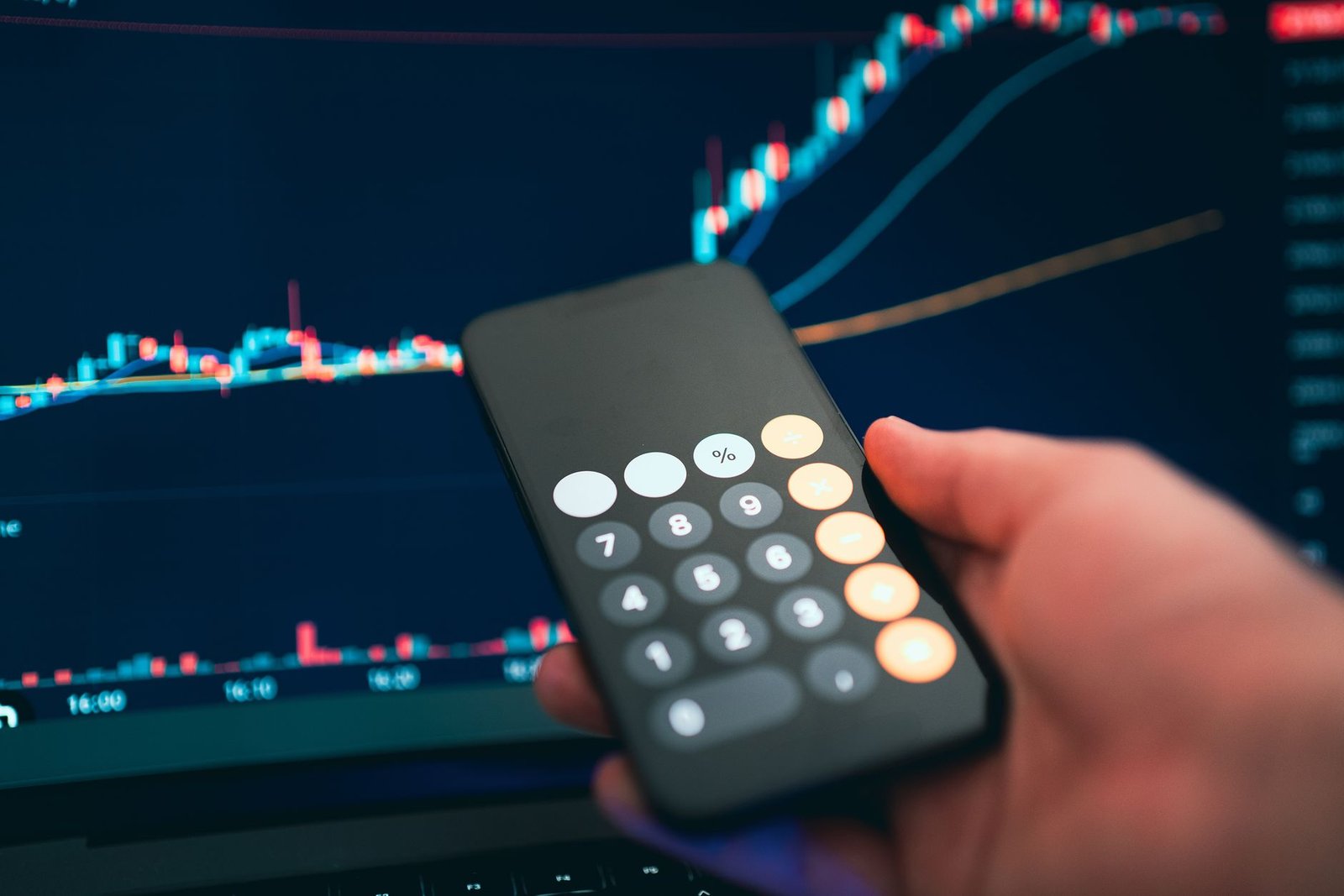 Close-up of a smartphone displaying a calculator with a financial chart in the background.