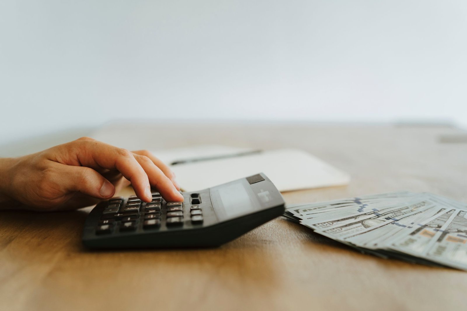 A hand calculating finances with a calculator next to stacks of US dollar bills.