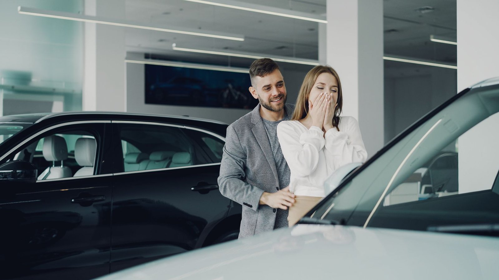 A joyful couple at a car dealership discovering their new car. Indoor setting, bright lighting.