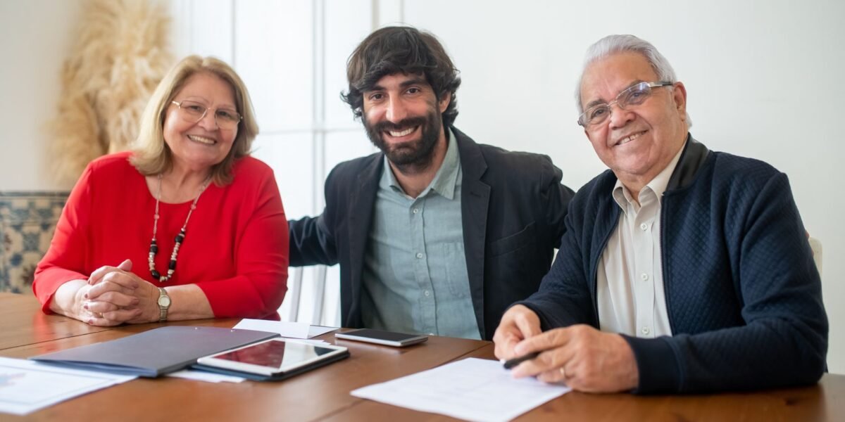 Group portrait of two senior adults and a young man smiling at a business meeting indoors.