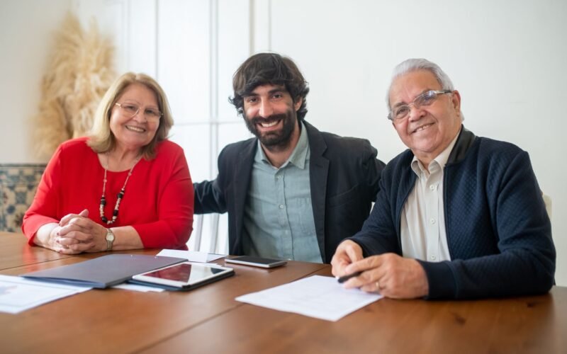 Group portrait of two senior adults and a young man smiling at a business meeting indoors.
