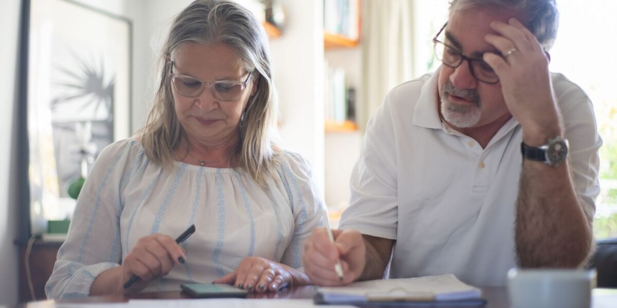 Senior couple calculating expenses at home office desk with documents and notes.