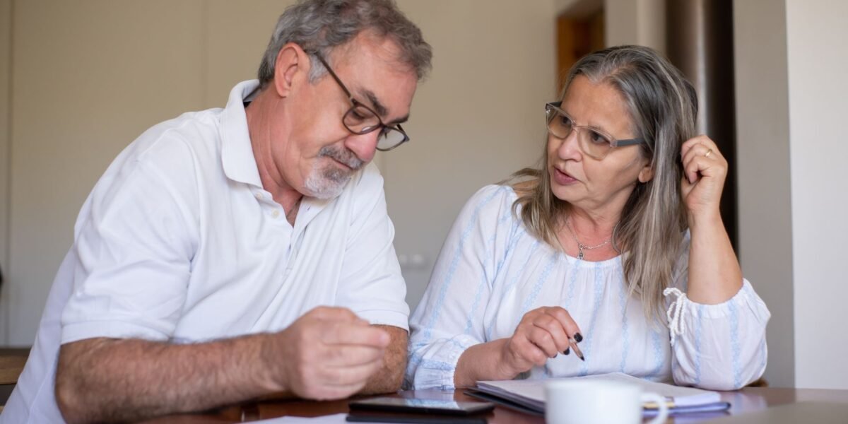 Senior couple reviewing documents and managing finances together at home, showing collaboration and care.