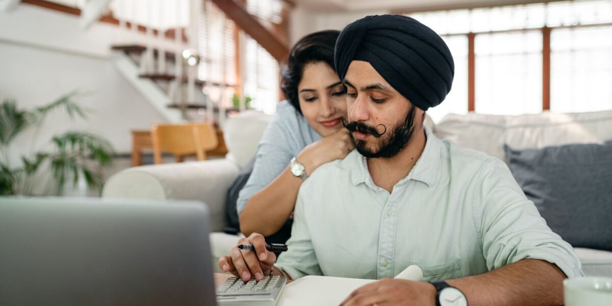 Young smiling woman hugging concentrated husband from behind while counting bills on calculator in modern apartment