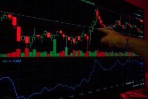 A hand points at a stock market graph on a digital screen, highlighting financial trading trends.