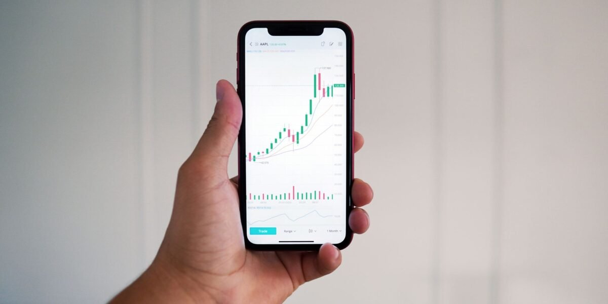 Close-up of a hand holding a smartphone showing a stock market chart indoors.