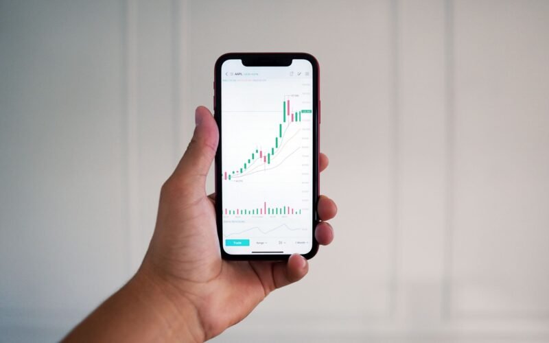 Close-up of a hand holding a smartphone showing a stock market chart indoors.