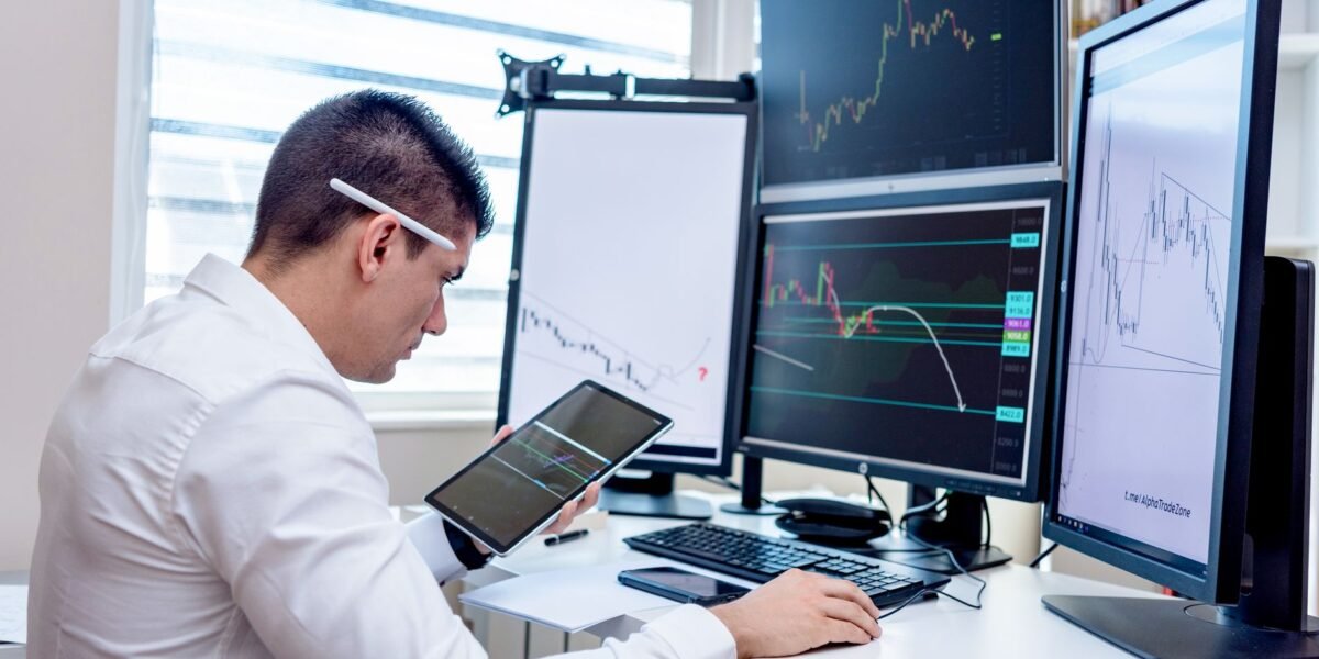 Professional analyzing stock market graphs on multiple monitors at work desk.