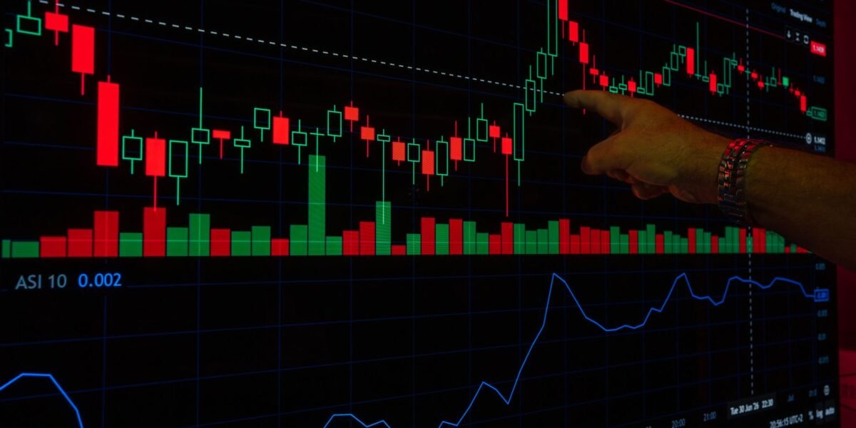 A hand points at a stock market graph on a digital screen, highlighting financial trading trends.