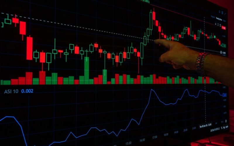 A hand points at a stock market graph on a digital screen, highlighting financial trading trends.