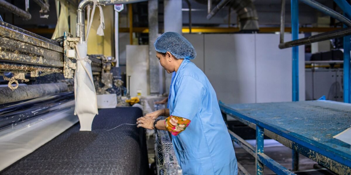 A female textile worker operates machinery in a factory, showcasing industrial production.