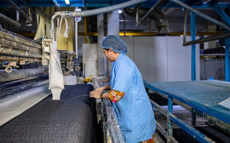 A female textile worker operates machinery in a factory, showcasing industrial production.