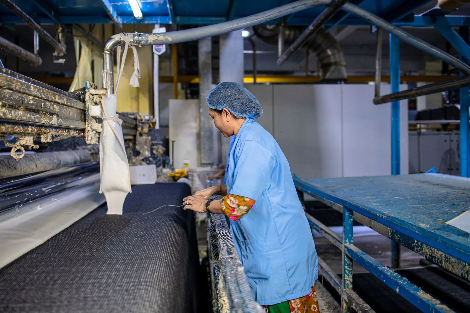 A female textile worker operates machinery in a factory, showcasing industrial production.