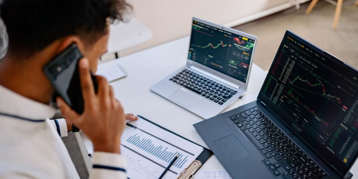 Man analyzing stock market charts on laptops while talking on a cellphone.