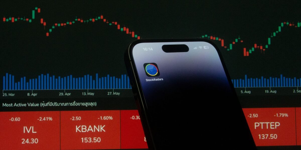 A mobile phone displaying a trading app in front of a financial market chart screen.