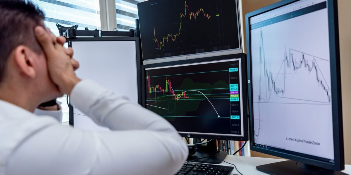 Frustrated man monitoring multiple trading graphs on computer screens in an office setting.