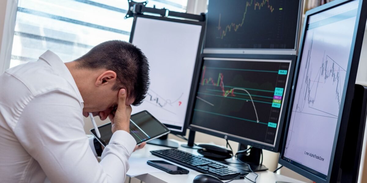 A stressed trader in an office setting analyzes market data on multiple monitors using a tablet.