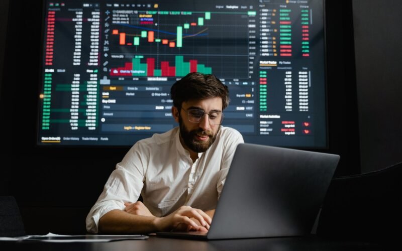Male analyst studies cryptocurrency trends at a workstation with multiple displays showing market data.