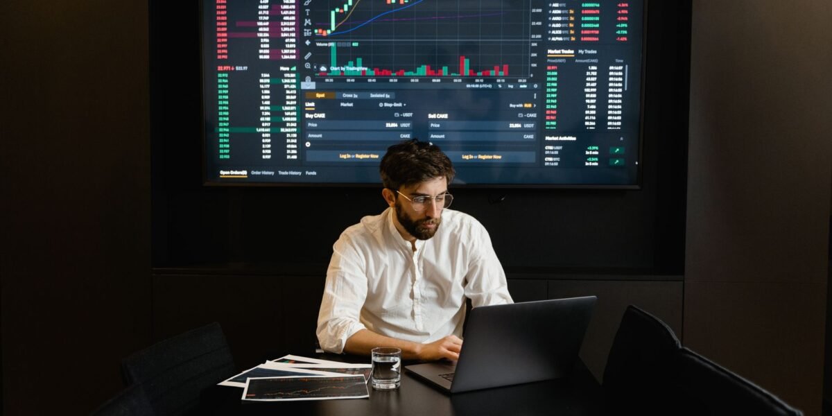 Focused businessman analyzing stock market data on laptop with financial graphs displayed on screen.