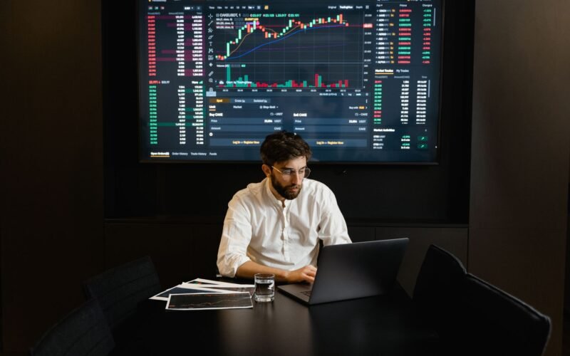 Focused businessman analyzing stock market data on laptop with financial graphs displayed on screen.