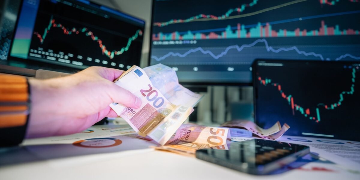 Close-up of euro banknotes with financial market graphs in the background, depicting finance and investment themes.