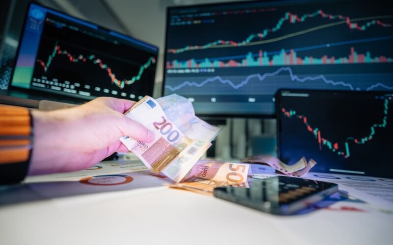 Close-up of euro banknotes with financial market graphs in the background, depicting finance and investment themes.