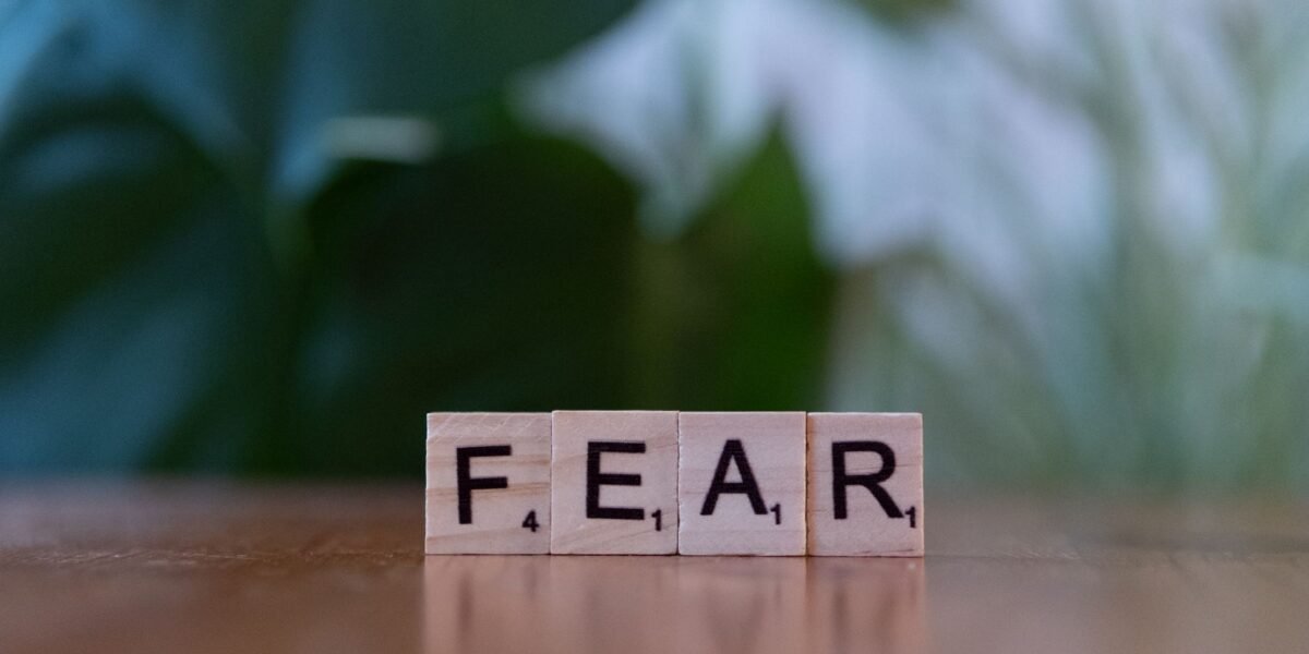 Wooden letter blocks spelling 'FEAR' on table against blurred green background. Emphasizes emotion and challenge.