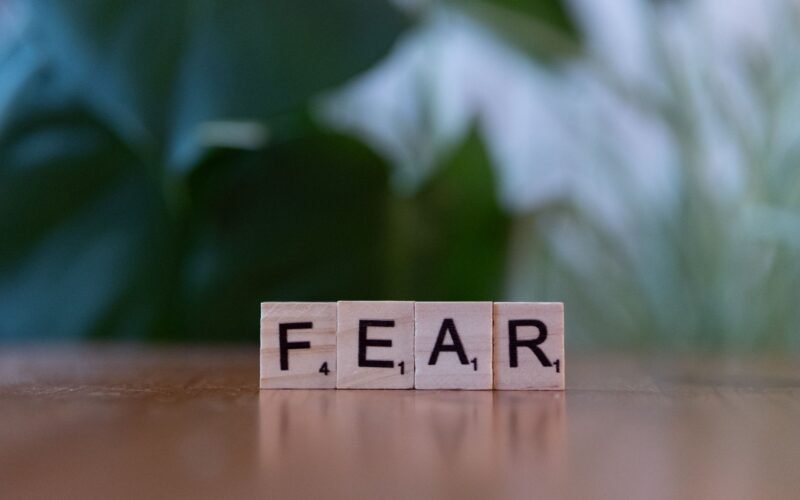 Wooden letter blocks spelling 'FEAR' on table against blurred green background. Emphasizes emotion and challenge.
