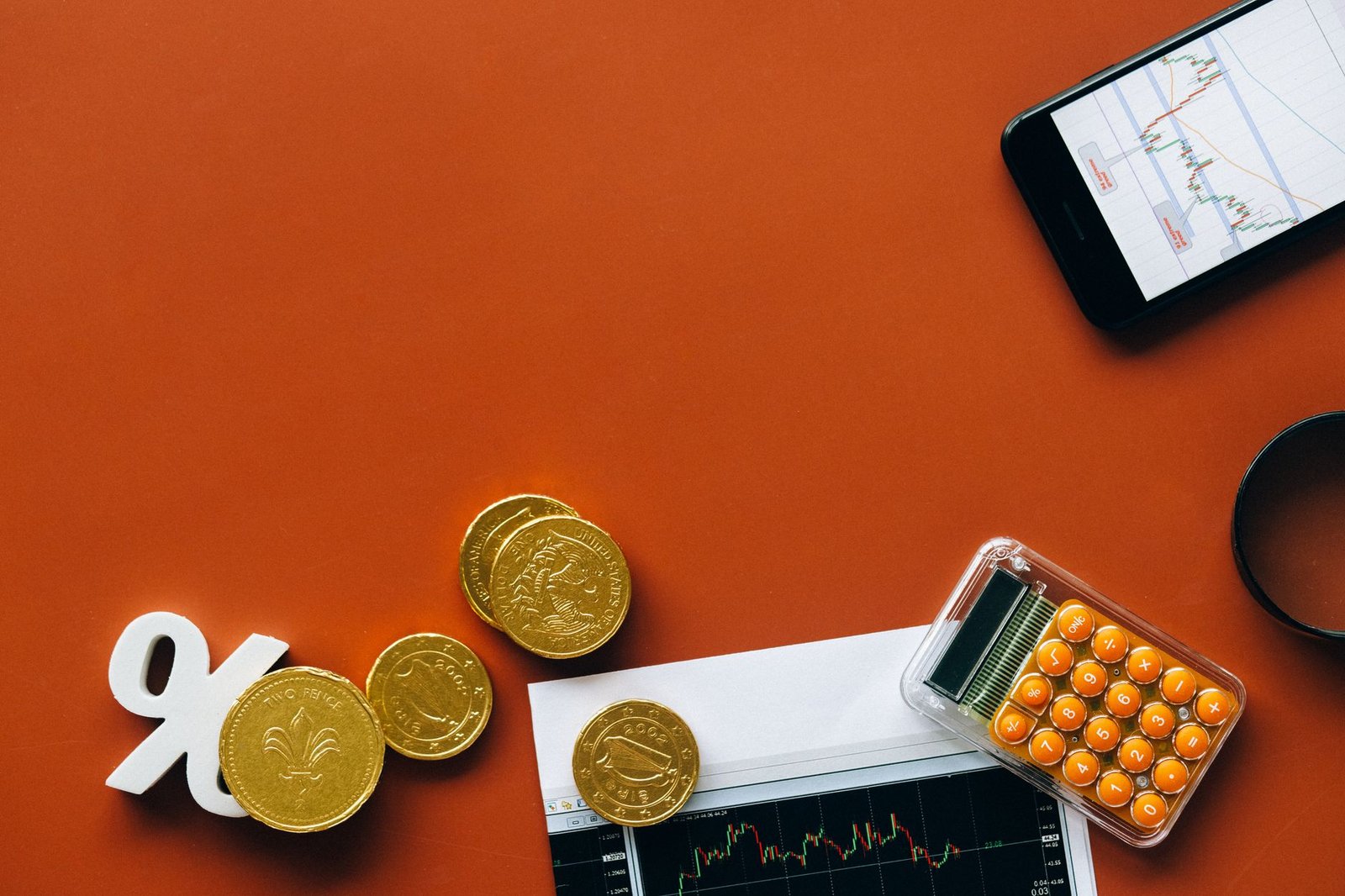 Flat lay showing coins, calculator, and charts on a red background for financial analysis and business concepts.