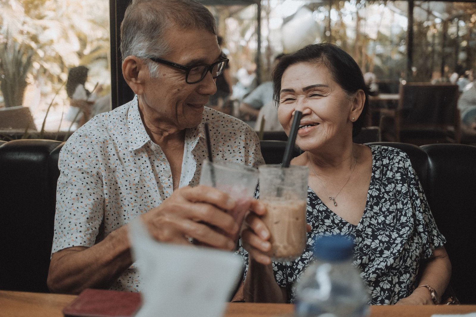 Happy senior couple sharing a moment with iced beverages in a cozy cafe setting.