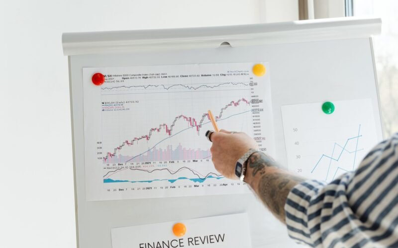 A tattooed person pointing at finance charts and graphs on a whiteboard.