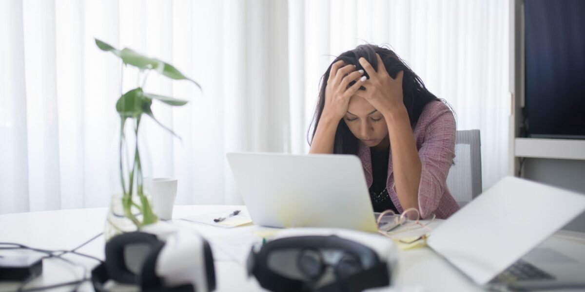Frustrated woman sitting at desk with laptop, showing stress in a modern office environment.