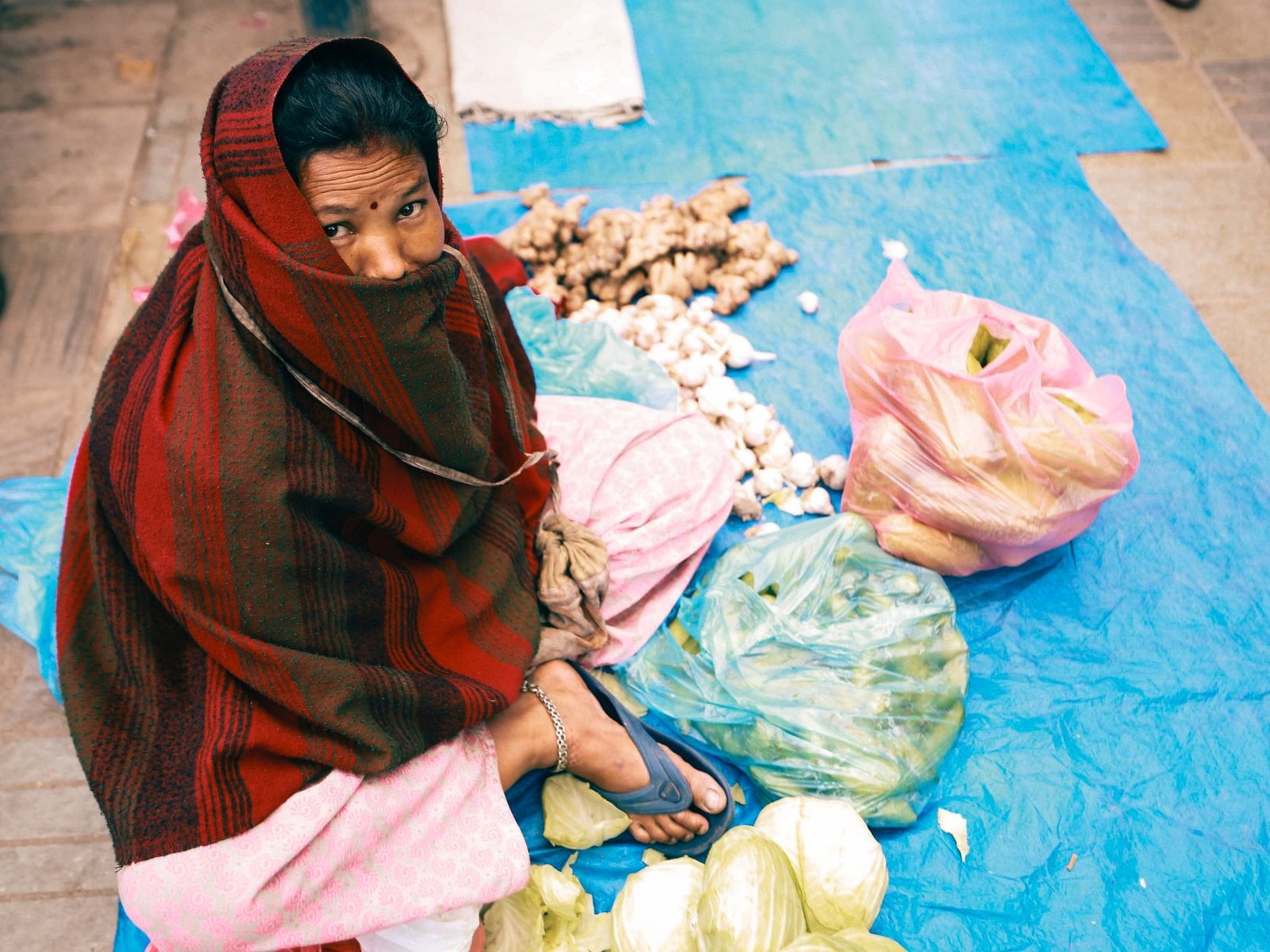 A woman in traditional attire selling vegetables on a city street.
