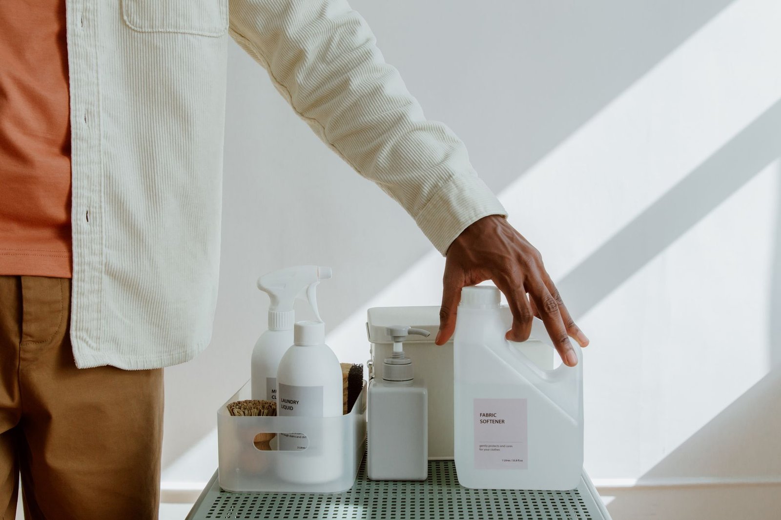 Close-up of a man holding fabric softener surrounded by cleaning products in a minimalist setting.