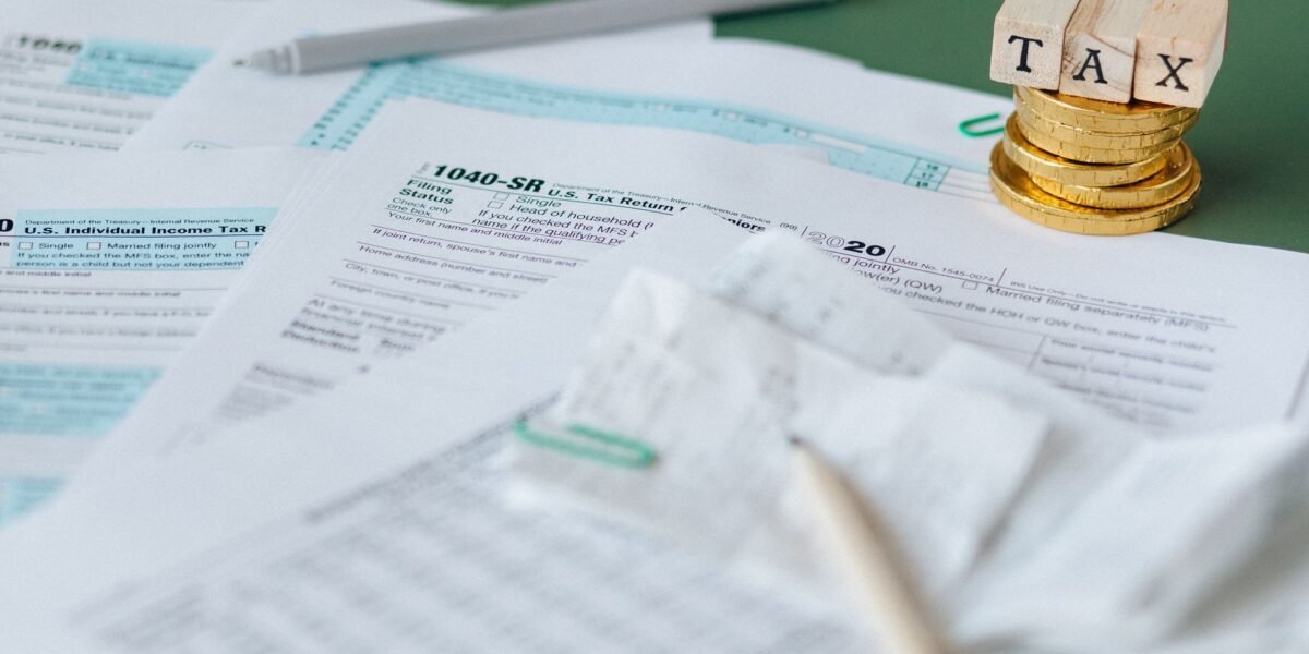 Stack of tax forms and coins with a 'TAX' stamp, symbolizing finance and accounting.