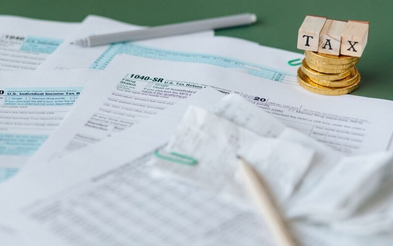 Stack of tax forms and coins with a 'TAX' stamp, symbolizing finance and accounting.