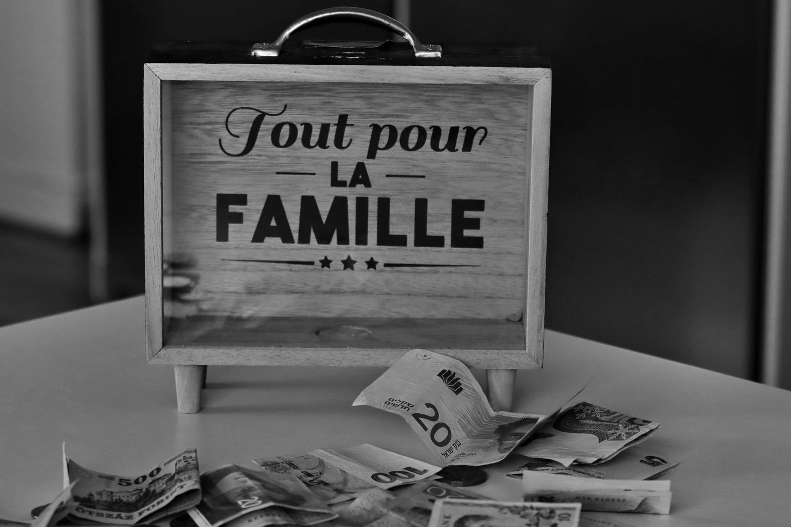 Black and white photo of a money box and various currencies on a table, symbolizing savings for family.