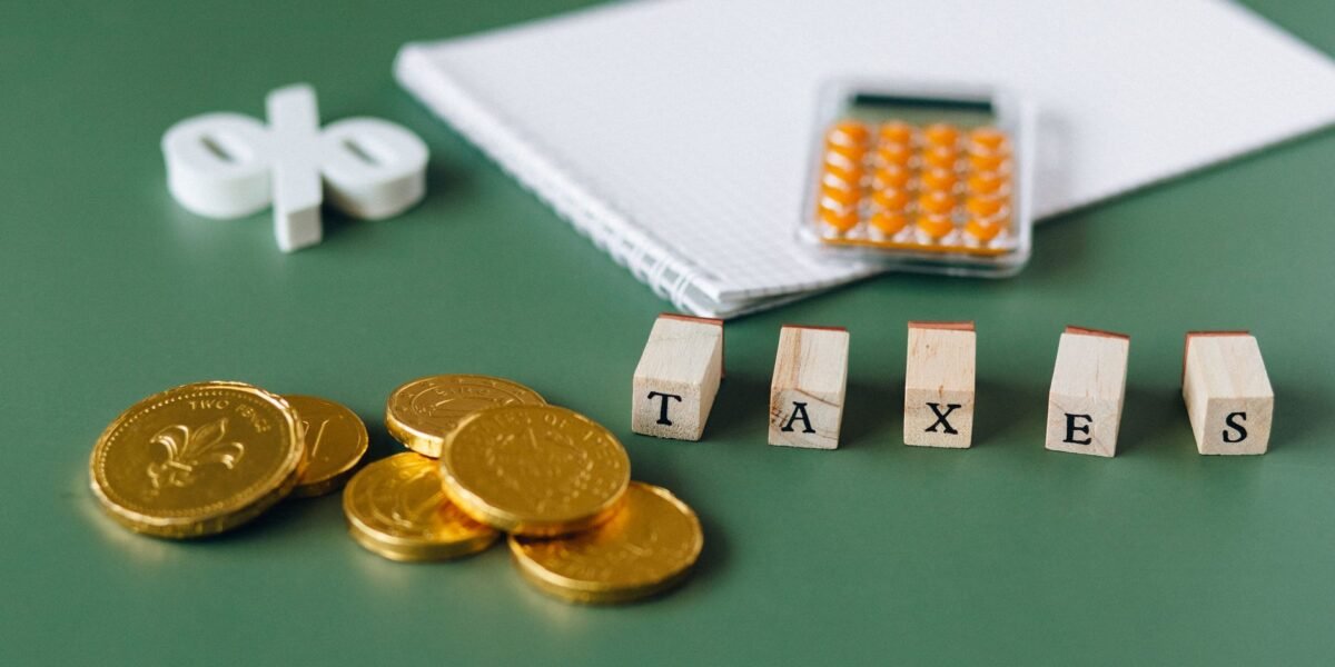 Close-up of tax-related items including coins, calculator, and word 'taxes' on a green background.