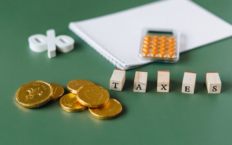 Close-up of tax-related items including coins, calculator, and word 'taxes' on a green background.