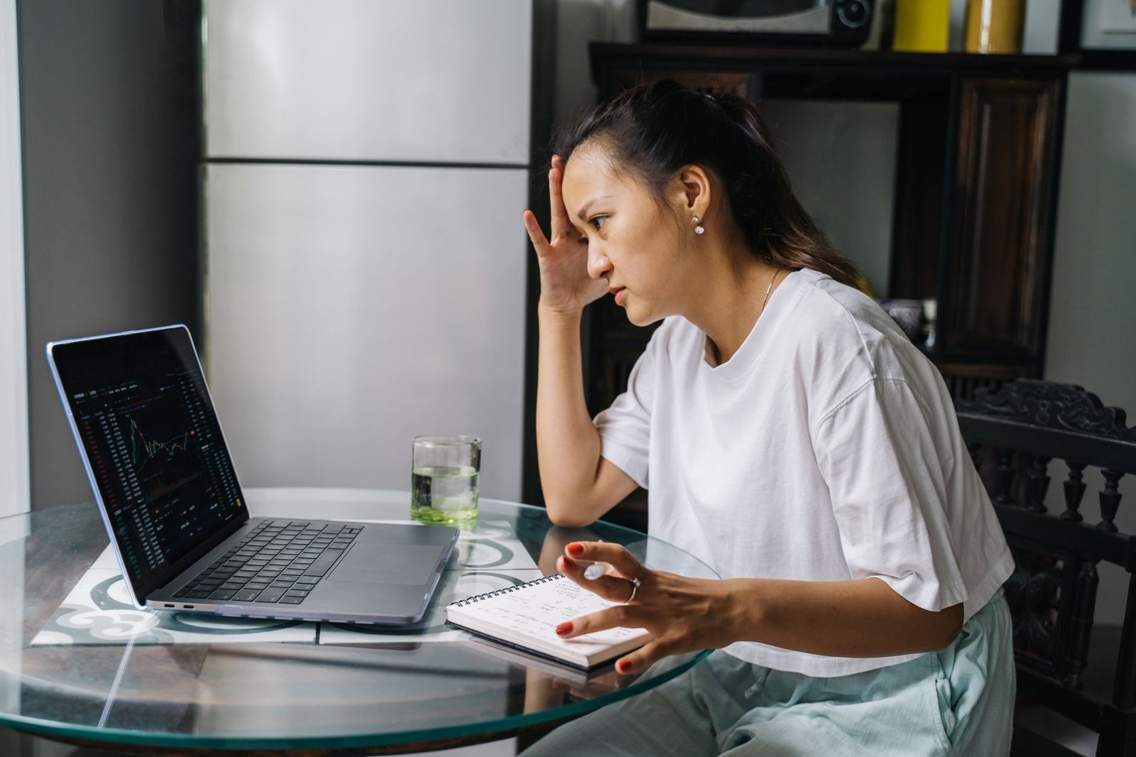 Woman worriedly analyzing stock market data on laptop at home, indicating financial stress.