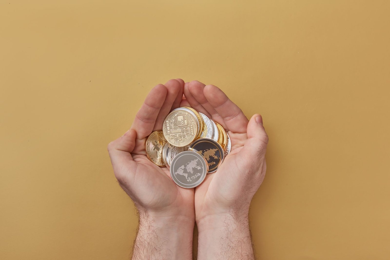 Close-up of hands holding various cryptocurrency coins over a yellow background, highlighting modern digital finance.