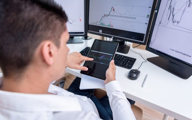 A stock trader analyzing cryptocurrency charts on multiple monitors and a tablet.