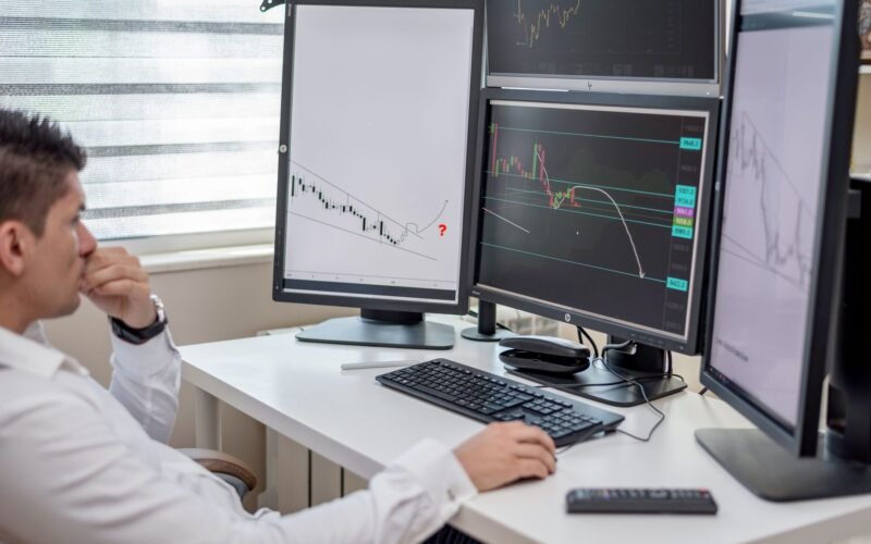 Business professional analyzing financial data on multiple computer monitors at his workspace.