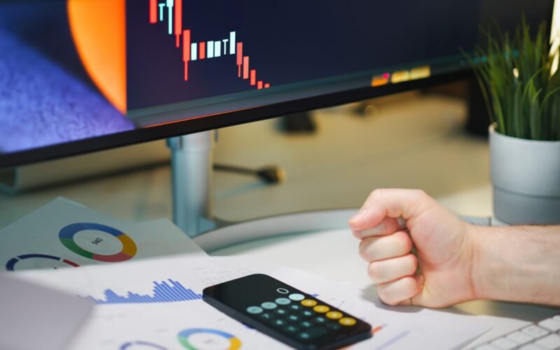 Close-up of a desk with financial graphs, a calculator, and a fist symbolizing determination.