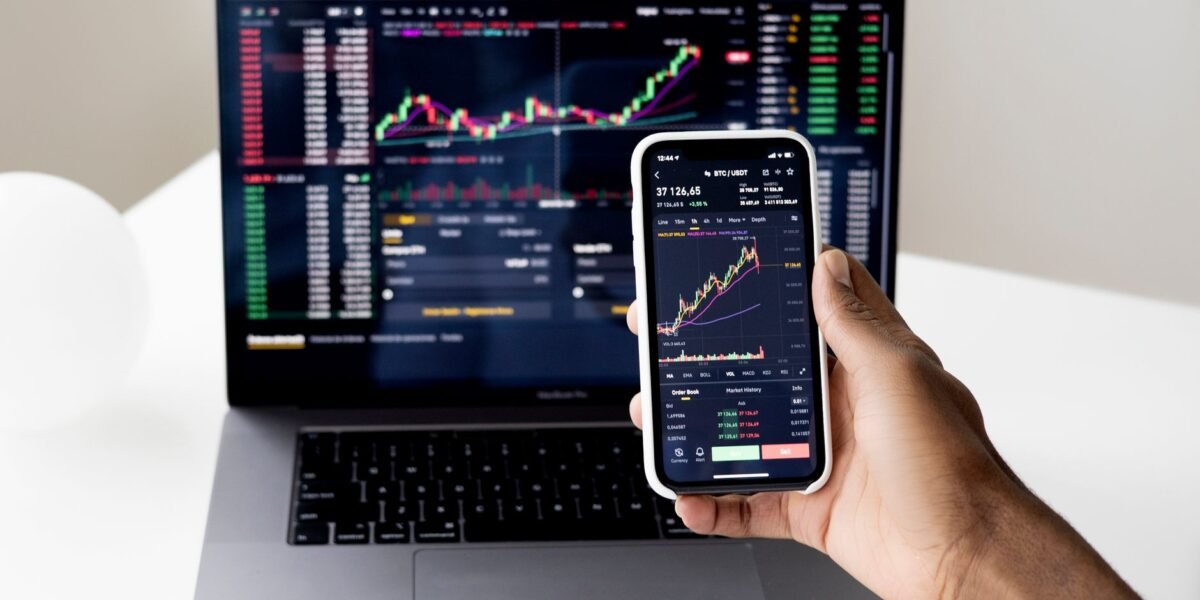 Person checking stock market graphs on laptop and smartphone, focusing on financial data.